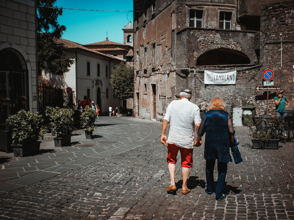 An elderly couple holding hands walking away down a cobbled street in Anagni, Italy