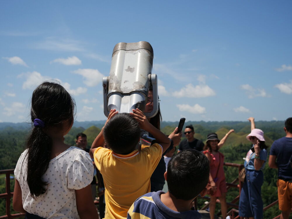 Children reaching up to coin-operated binoculars at the Chocolate Hills viewpoint, Bohol, Philippines
