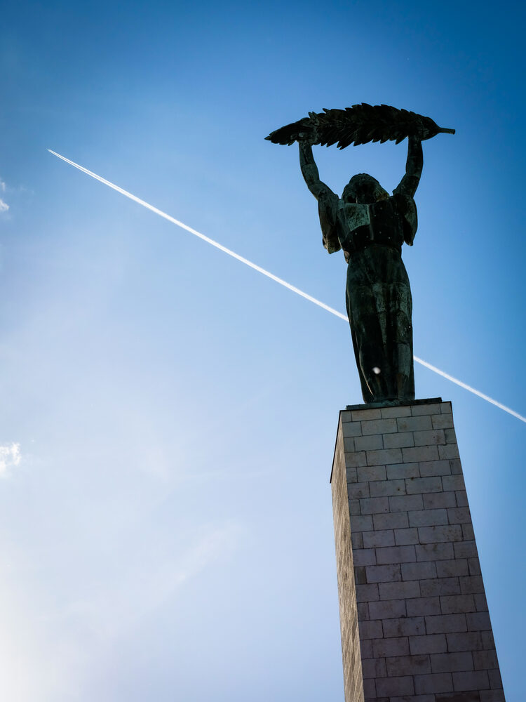 Liberty Statue on Gellert Hill against a blue sky crossed by a jet contrail, Budapest