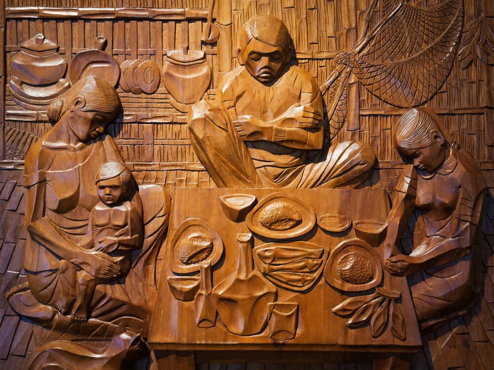 Carved wooden relief of a family with bowed heads saying grace around a table with fish, Cebu, Philippines