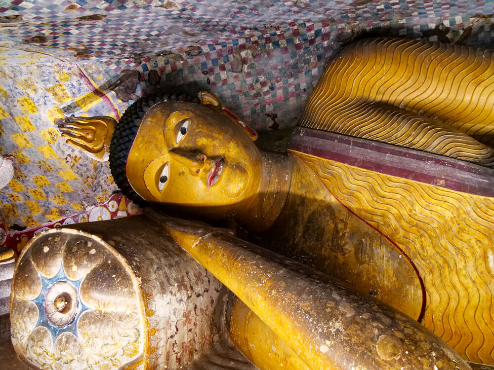 A golden reclining Buddha statue beneath a painted checkered cave ceiling at Dambulla, Sri Lanka