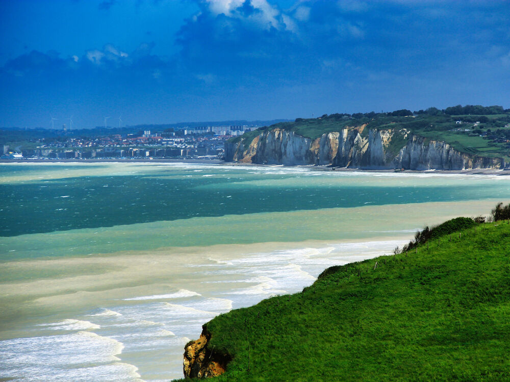 White chalk cliffs and a coastal town seen across a wide bay, with wind turbines on the hill behind, Dieppe