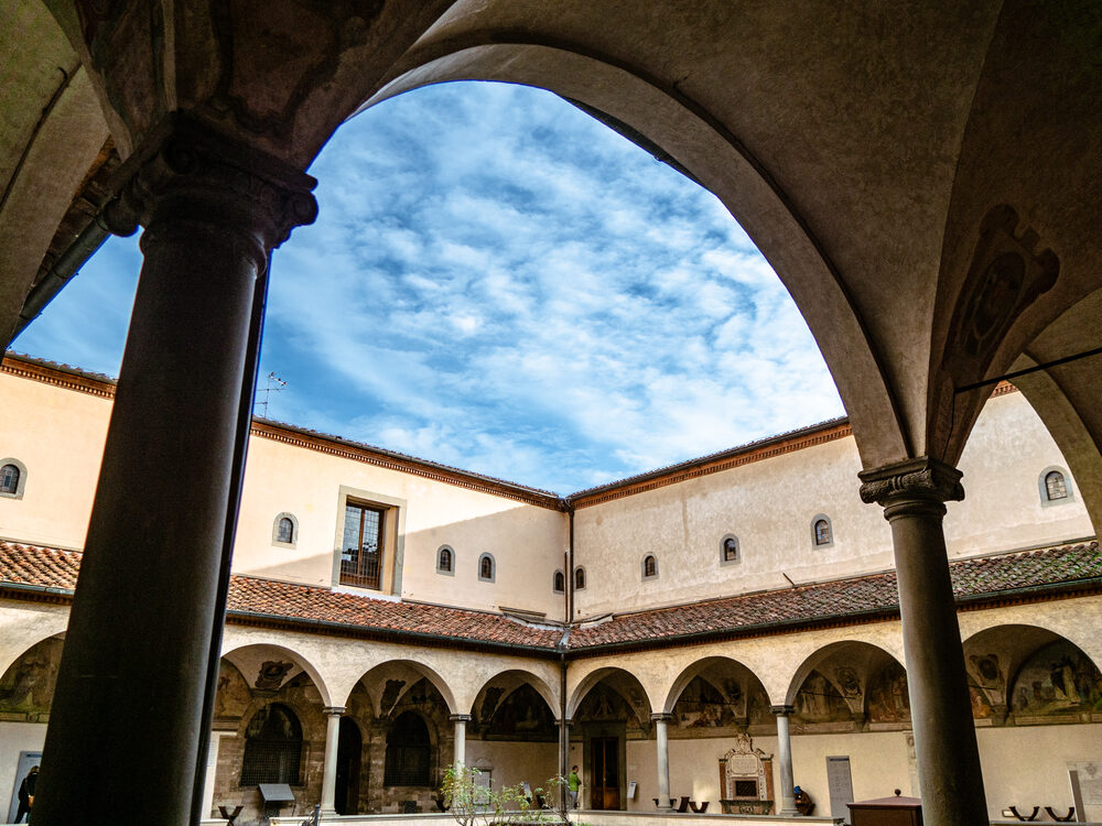 Cloister arches framing a bright, cloud-streaked sky, Florence