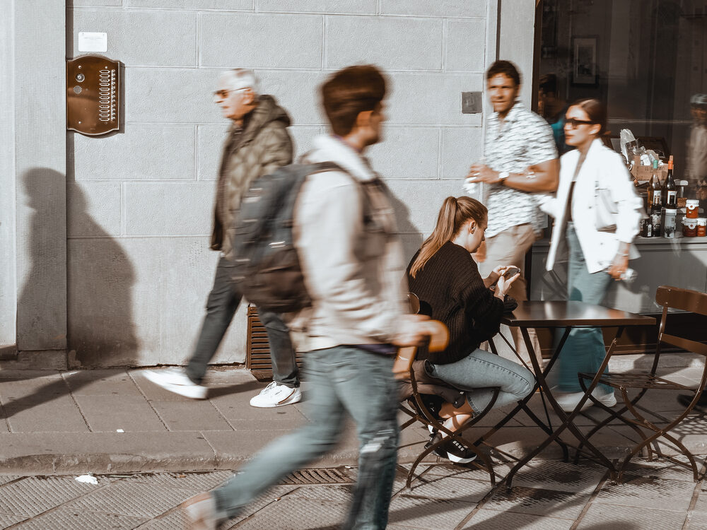Blurred passersby on a sunlit Florence street with one seated person in sharp focus