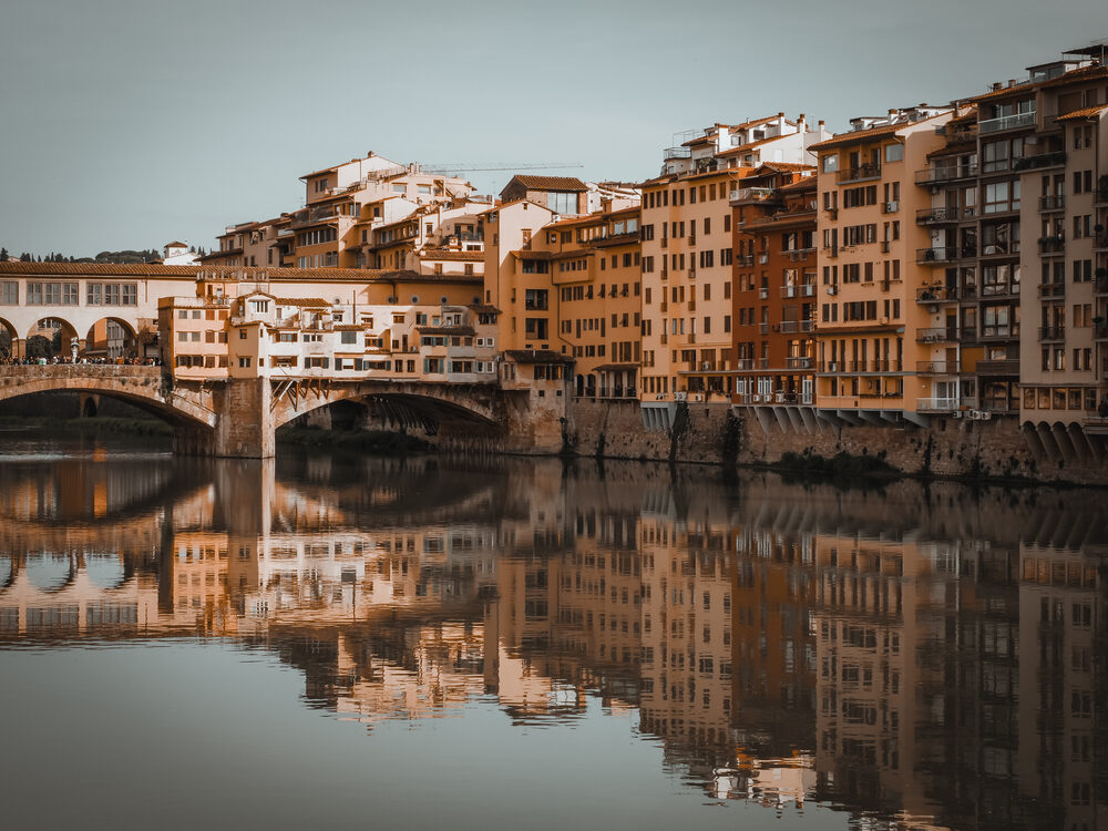 Ponte Vecchio and its reflection in the calm Arno at golden hour, Florence