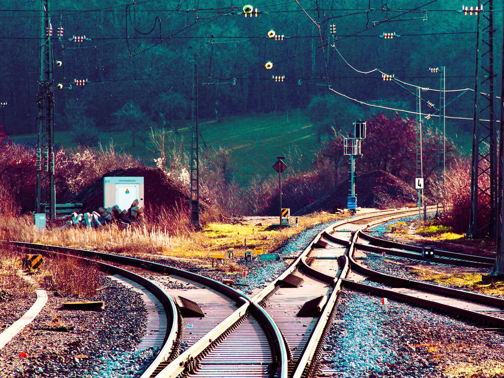 Railway tracks converging at a set of points with overhead wires and a wooded hillside behind, Germany