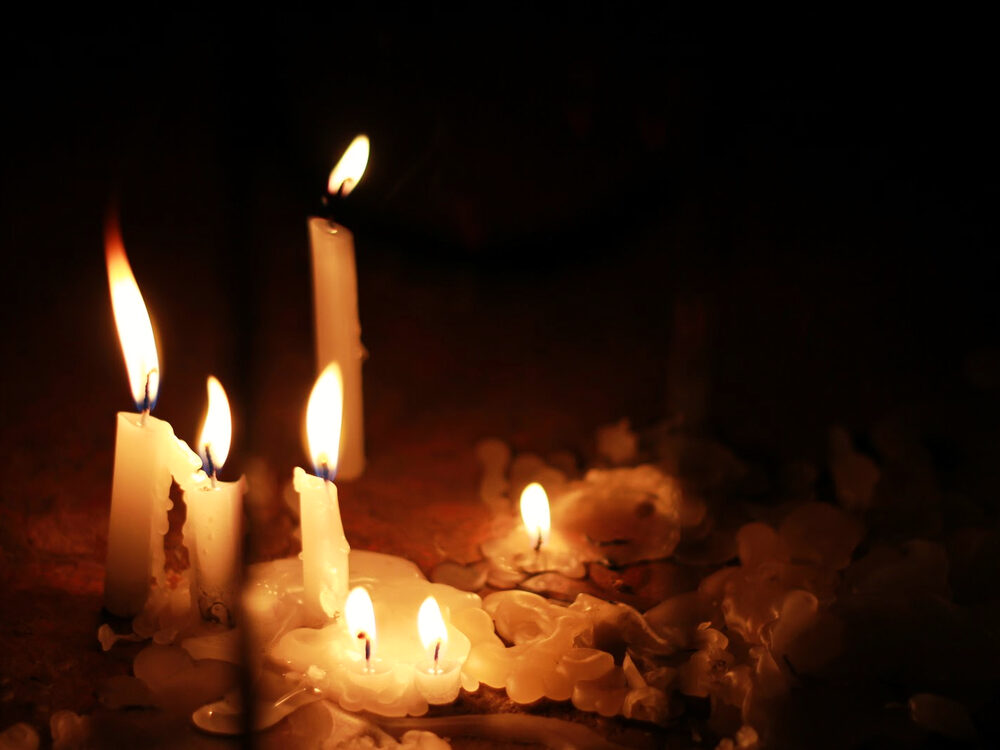 Several white candles burning with pooled melted wax against a dark background, India