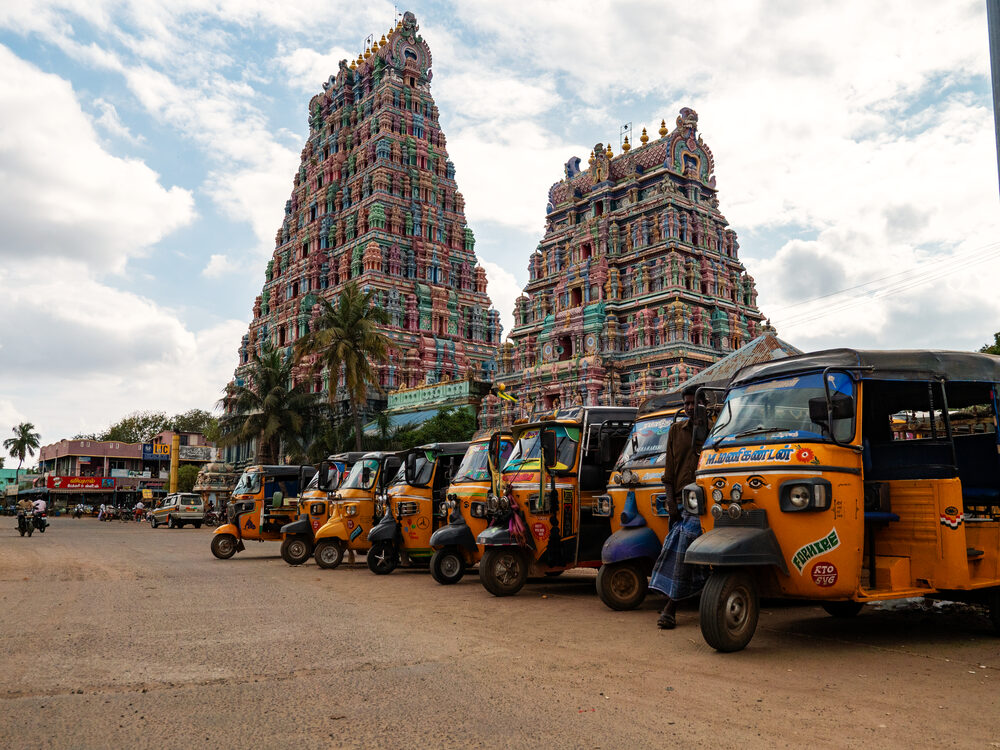 Row of yellow auto-rickshaws parked before two tall, colourful Hindu temple gopurams, Tamil Nadu