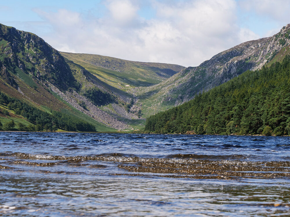 Glendalough Upper Lake between green and rocky mountains under a bright sky, County Wicklow, Ireland