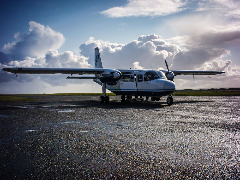 A small twin-propeller Islander aircraft on wet tarmac under dramatic clouds, Ireland