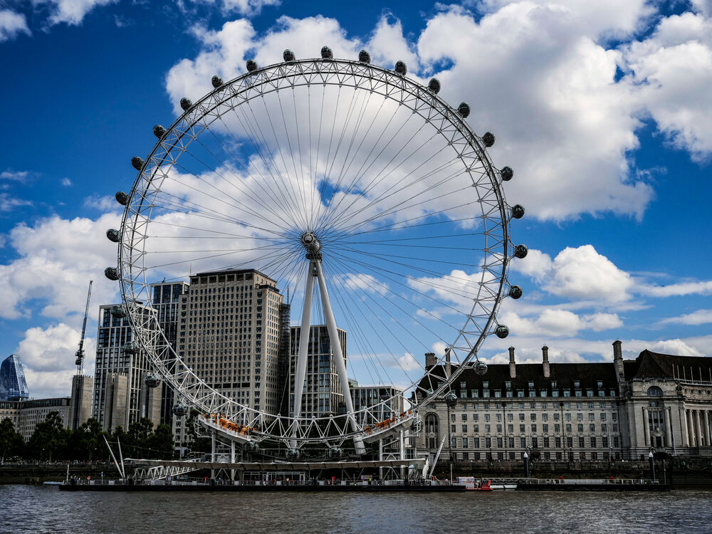 The full circle of the London Eye against blue sky and clouds with County Hall beside it