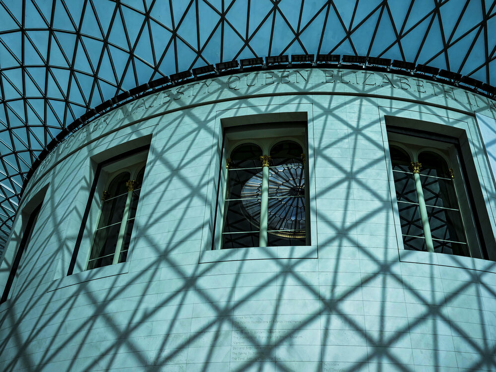 The British Museum Great Court's glass lattice roof casting diagonal shadows on the curved Reading Room wall