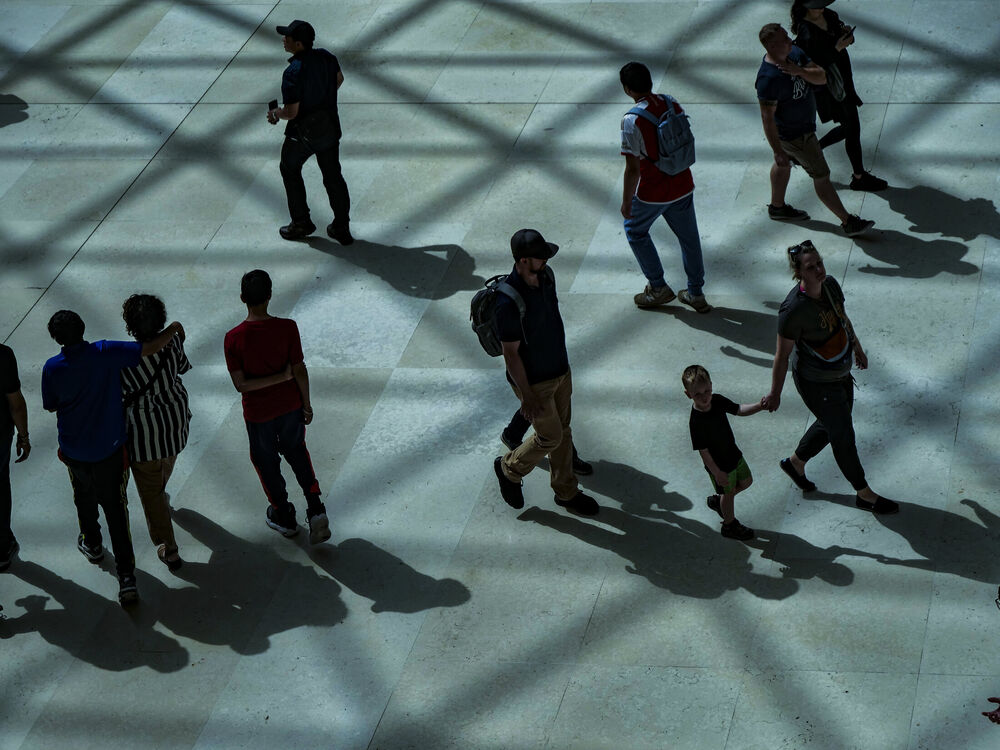 Visitors seen from above crossing the British Museum Great Court floor through a net of lattice shadows