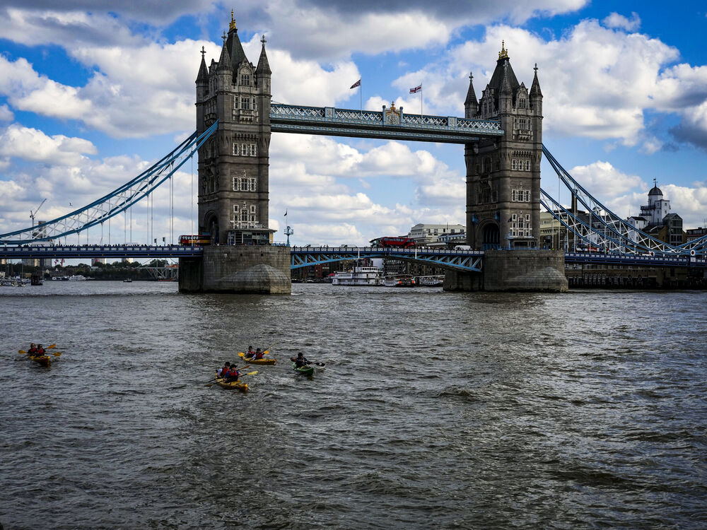 Tower Bridge over the Thames with kayakers paddling in the foreground under a cloudy blue sky, London