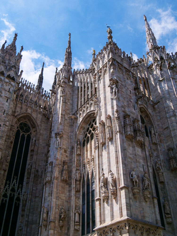 The Gothic spires and pinnacles of Milan Cathedral rising against a blue sky with light clouds