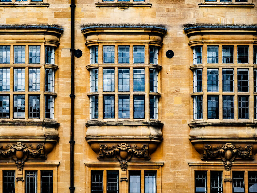 Symmetrical stone bay windows with leaded panes on an Oxford college facade