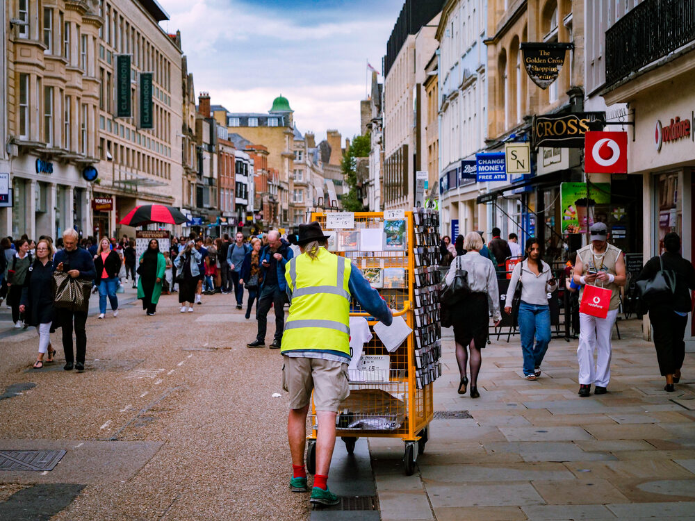 Vendor pushing a postcard cart through a busy Oxford shopping street