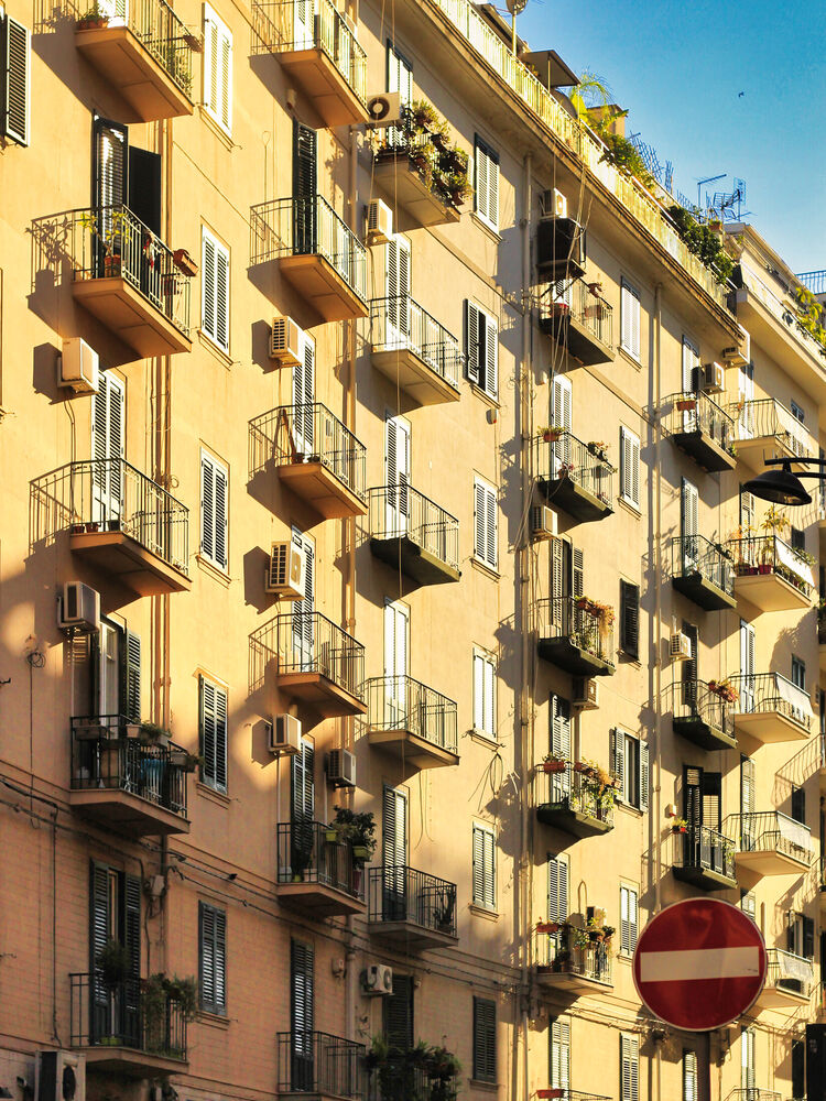 Sunlit apartment facade with rows of balconies, shutters and air conditioners, Palermo