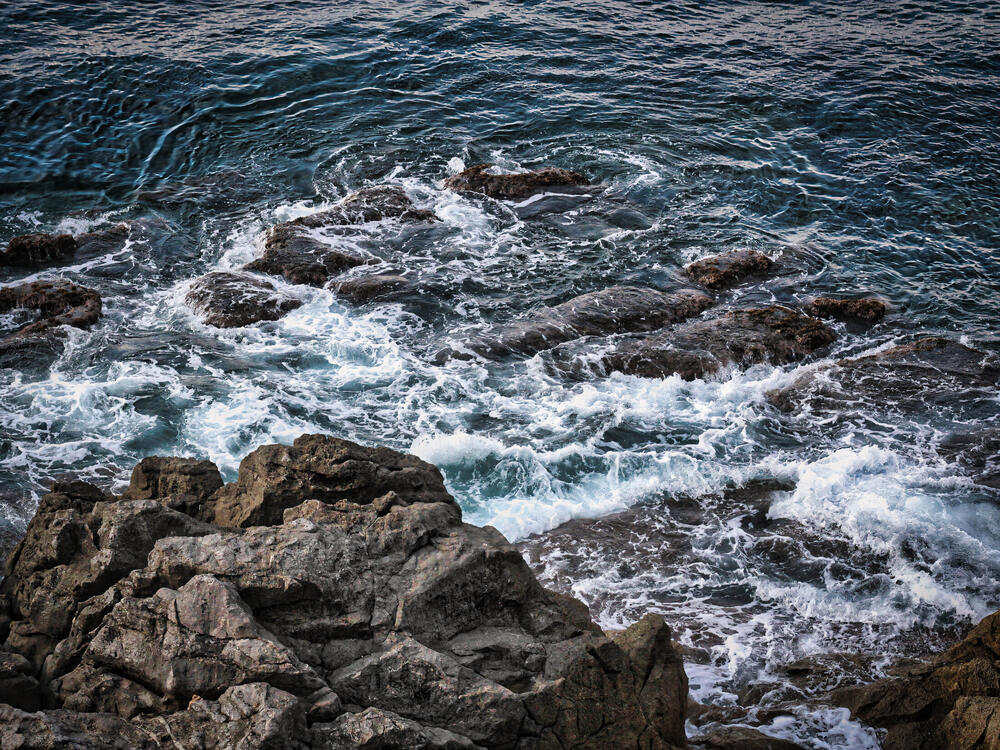 White surf churning over dark flat rocks seen from above on the Palermo coast