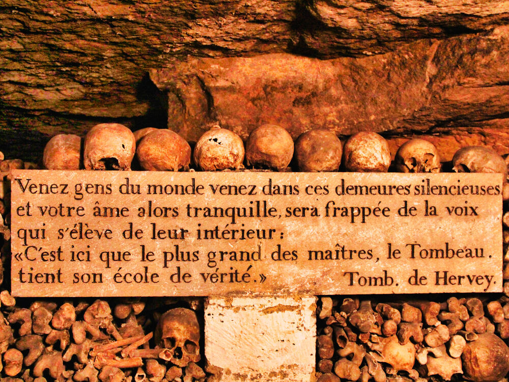 Rows of skulls above a carved stone plaque bearing a nineteenth-century French inscription, Paris Catacombs
