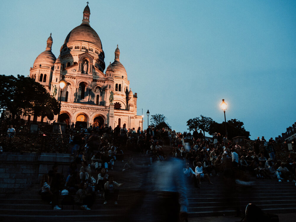 Sacré-Cœur basilica illuminated at dusk with crowds sitting on the steps below, Montmartre, Paris