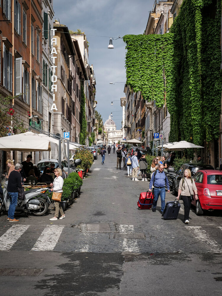 A Monti street in Rome with trattoria sign, ivy wall, cafe terraces and the dome of Santa Maria Maggiore beyond