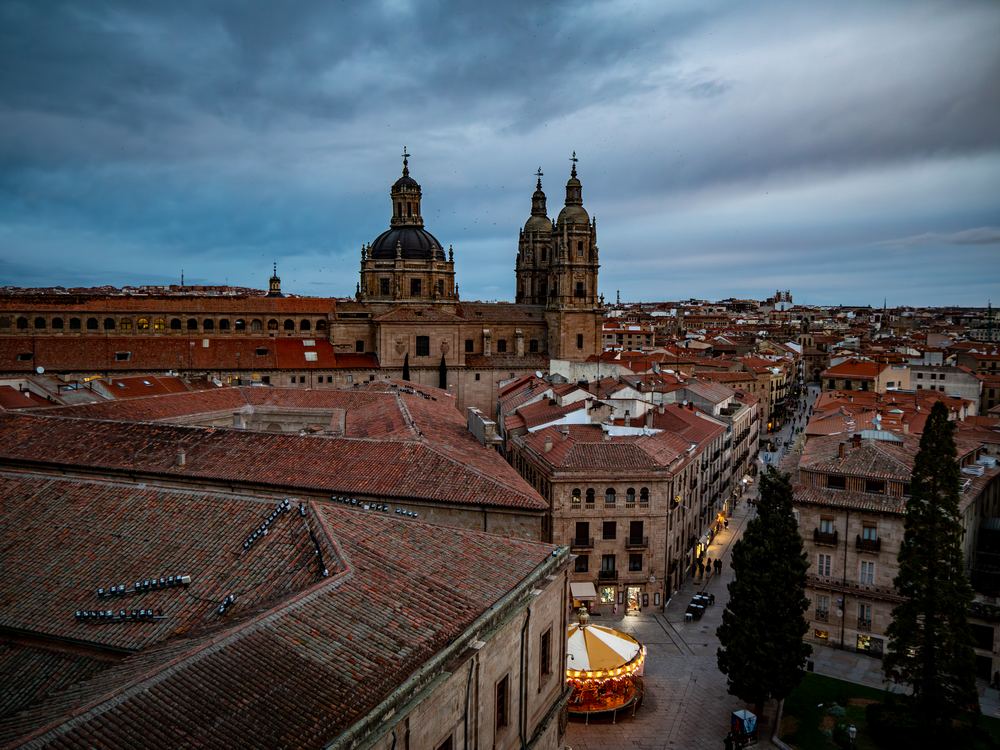 Salamanca skyline at dusk with cathedral towers and a lit carousel