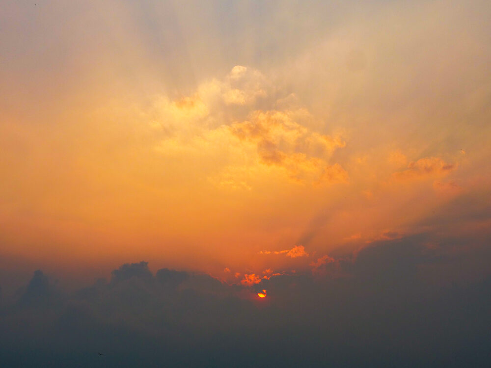 Hazy orange sunset with the sun breaking through cloud over the Western Ghats, Thekkady