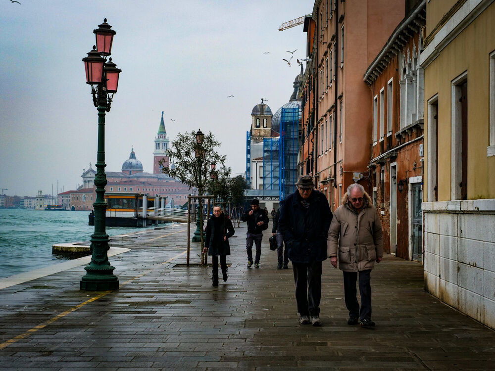 People in winter coats walking along the Giudecca waterfront promenade with San Giorgio Maggiore behind, Venice