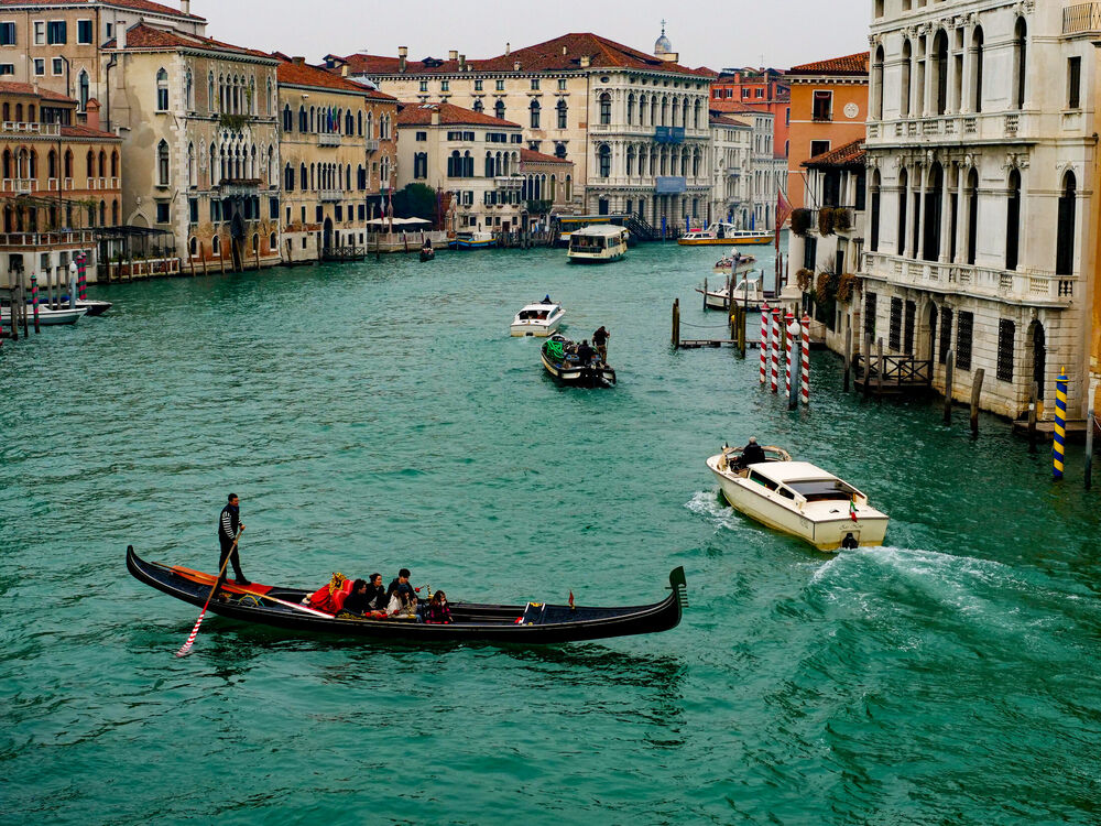 A gondola with passengers crossing the Grand Canal among water taxis and work boats, Venice