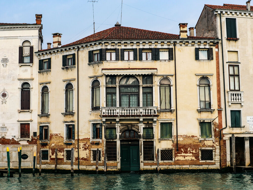 A weathered Venetian palazzo facade with arched windows and peeling plaster rising from canal water