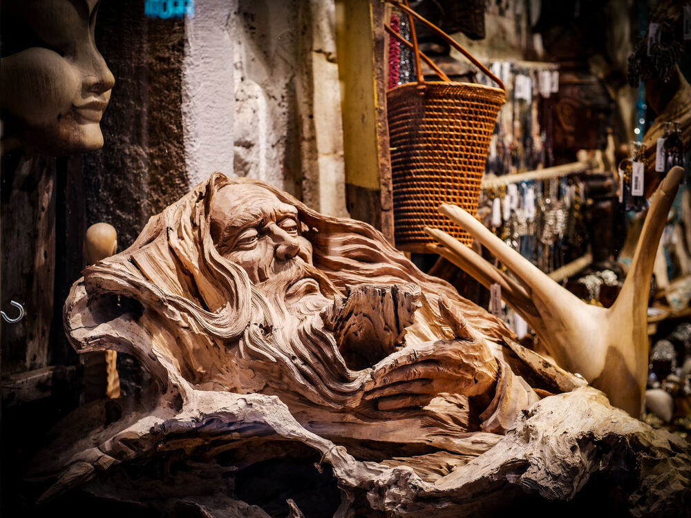 A carved wooden sculpture of an old bearded face emerging from driftwood in a Venetian shop window