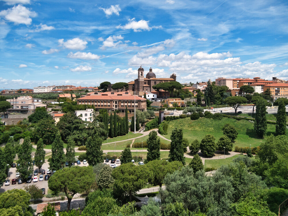 Panorama of Viterbo with a domed church, umbrella pines and a green park under a blue sky