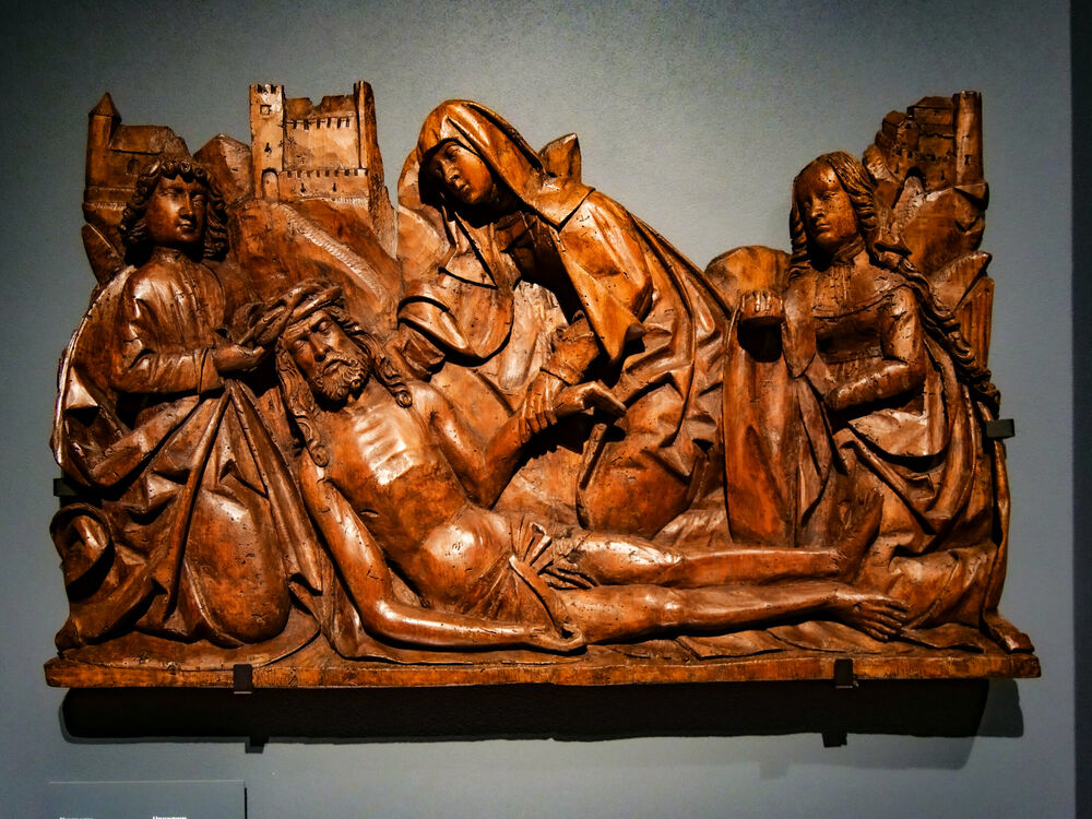 Medieval carved wooden relief of the Lamentation of Christ displayed on a museum wall, Warsaw